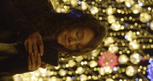 Young woman with smartphone chatting online. Young woman on the street in the light of festive lights on the Christmas eve. She chatting with friends online and listening to music. Slow motion video.
