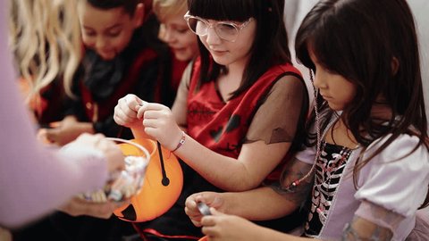 Group of kids wearing halloween costume receiving candies in pumpkin basket at home วิดีโอสต็อก