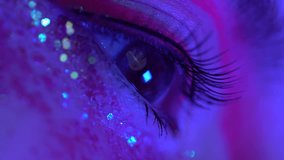 Extreme close-up view of opens and closes female eye with stage make-up with sequins and arrows. Cinematic shot of female eye illuminated colored neon lighting. Selective focus, handheld. Part series - Powered by Shutterstock - Get 15% off with code: PIKWIZARD15