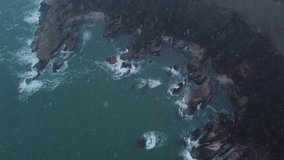 Aerial 4k video with drone on rocky beach with winter season and falling snow in sardala bay