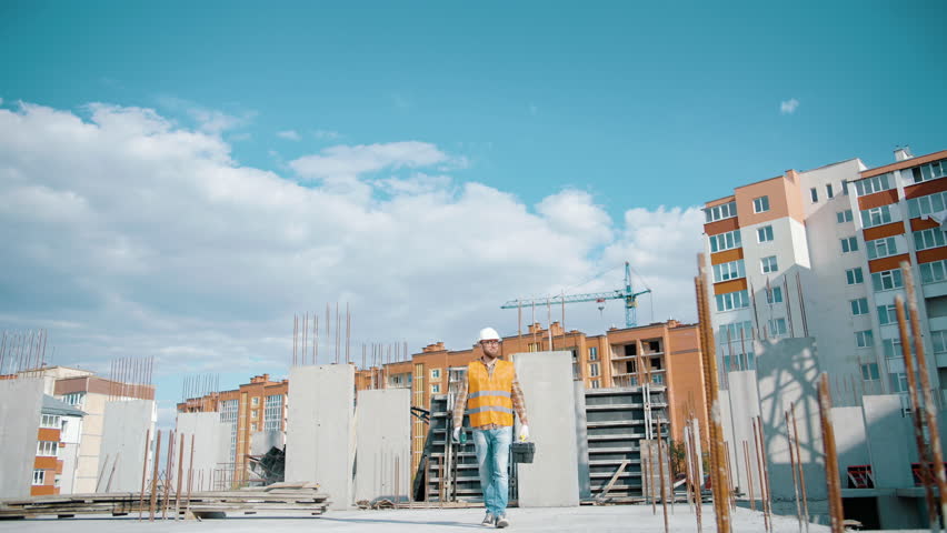 Construction worker walking and working on a construction site with a toolbox and screwdriver and high visibility clothing. Slow motion Royalty-Free Stock Footage #1103802637