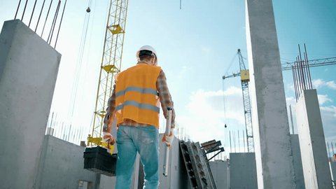 Construction worker walking and working on a construction site with a toolbox and bubble level and high visibility clothing. Man turns to the camera Video de stock