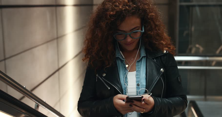 Laughing young woman listening to music on her cellphone while riding up an escalator in a metro station Royalty-Free Stock Footage #1103805875