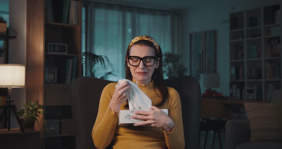 Emotional woman watching a romatic drama movie on TV, she is crying and blowing her nose on tissues | Shutterstock HD Video #1103810825
