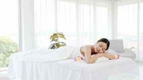 Relaxing young woman lying down and closed her eyes on massage beds at Asian luxury spa salon with white linen and wellness center, waiting for receiving massage from therapist. Spa salon concept