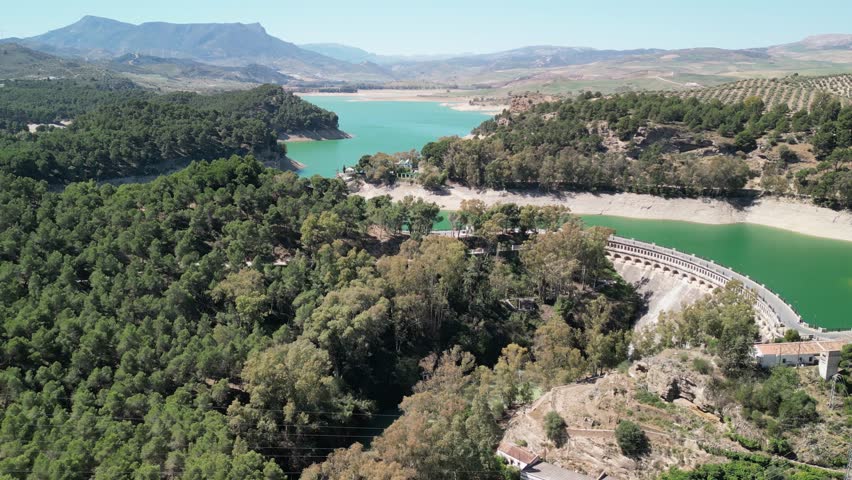 Panning drone clip of El Chorro hydroelectric dam with forested hilly landscape in the background