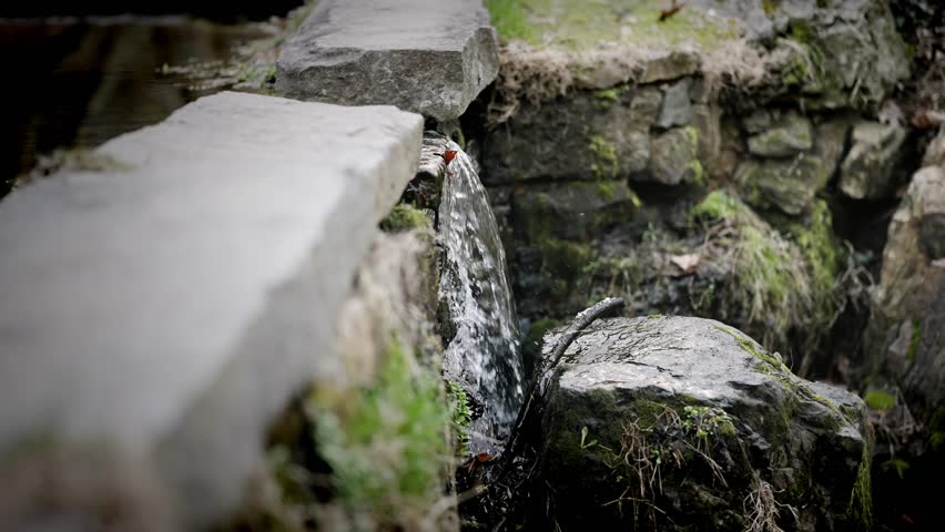 Medium view of water spilling through granite rock wall in pond, slow motion - Powered by Shutterstock - Get 15% off with code: PIKWIZARD15