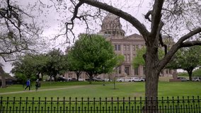 Texas state capitol building in Austin, Texas with gimbal video waking sideways with trees and fence in foreground.