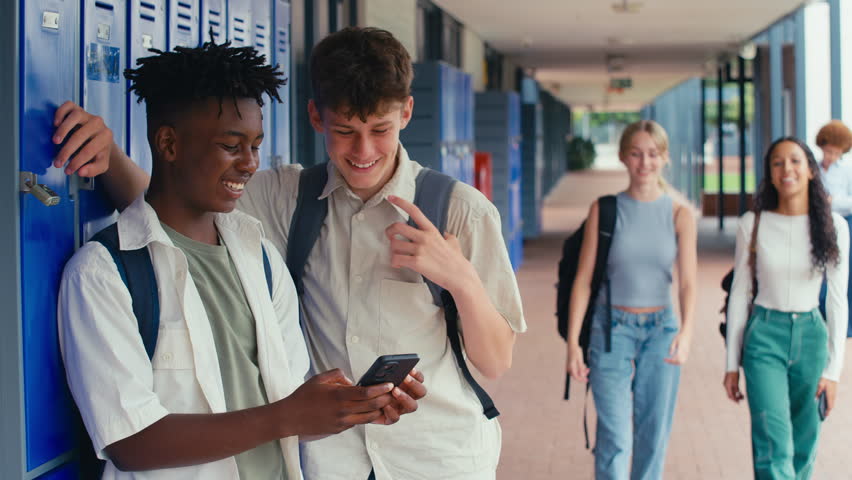 Two male high school or secondary students looking at social media or internet on mobile phone by lockers - shot in slow motion
