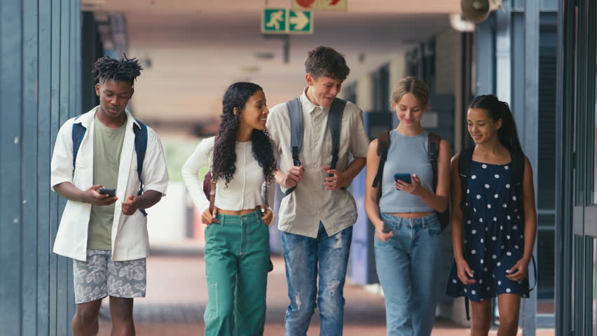 Multi-cultural class of high school students walking outside classrooms looking at mobile phones - shot in slow motion