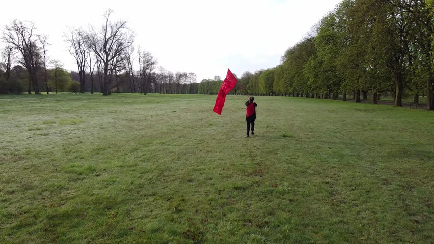 slow motion shot of a person running across a meadow with a red flag