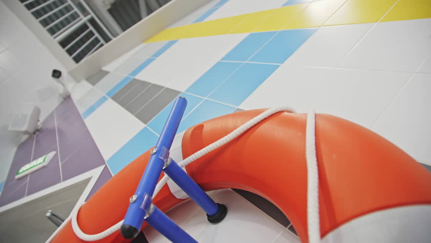 Life preserver ring hangs on tiled wall in modern swimming pool hall closeup. Safety equipment prepared for visitors in sports center Royalty-Free Stock Footage #1103827045