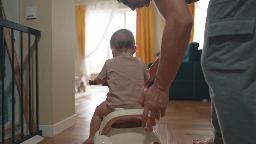 baby rides a motor scooter indoors. dad rides his son teaches him to ride a scooter around the room at home. happy family kid lifestyle dream concept. parent play baby rides scooter plays indoors Royalty-Free Stock Footage #1103827879