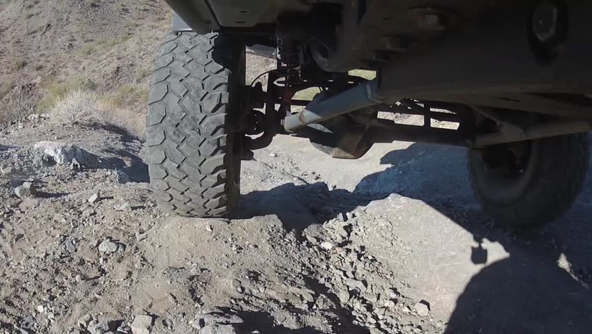 POV style shot from underneath a 4x4 vehicle, showing the suspension traveling and working over rough terrain. Vehicle is traveling downhill, in a desert setting. Royalty-Free Stock Footage #1103830839