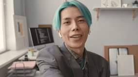Handheld POV of Asian gen z male programmer with colored blue hair recording video blog at workplace in modern office