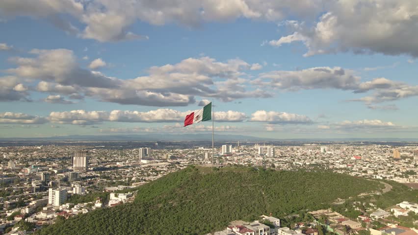 4K aerial drone view of the Mexican flag waving on Cerro del Obispado in Monterrey, Mexico. Ideal for themes of Mexican Independence Day, patriotism, tourism, and cultural celebrations.