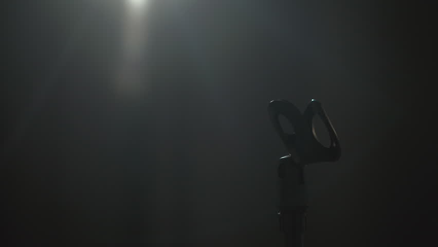 Close up microphone Attractive singer woman singing music on stage with spotlight strike through the darkness at concert event. Beautiful female musician performing live with light and smoke at hall.