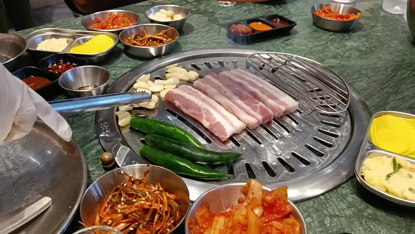 Korean BBQ Grill. Close-up view on the grill roasting pork Garlic and green peppers are cutting fresh to roast on the stove.