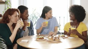 Multiethnic friends drinking orange juice while eating breakfast together
