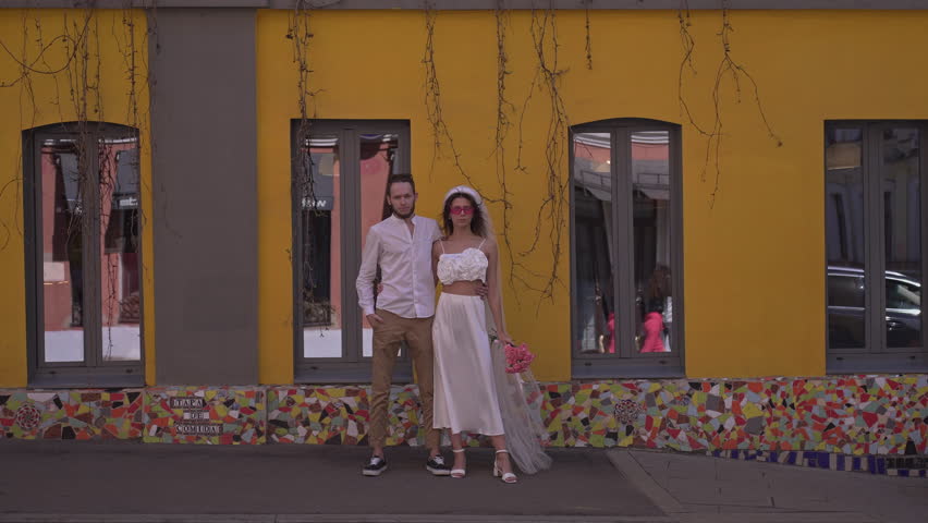 bride and groom stand against the background of a yellow building embracing