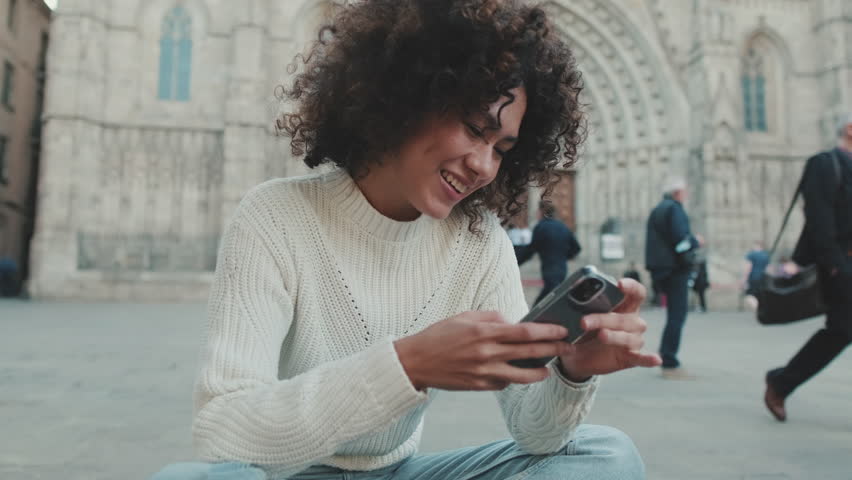 Young woman scrolls on a cell phone. Happy girl uses mobile phone on old city background