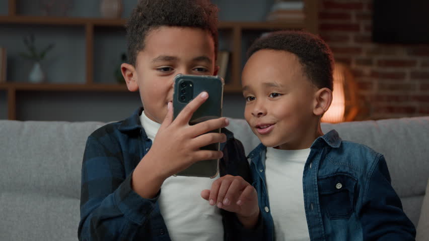 Two little siblings boys African American kids sons friends children brothers has video call online chat virtual meeting with smartphone technology app at home greeting hello to cell phone web camera Royalty-Free Stock Footage #1103849825