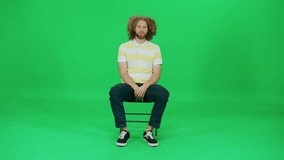 Focused man sitting on a chair and waiting, a man with an afro hairstyle, green background, chroma key template.