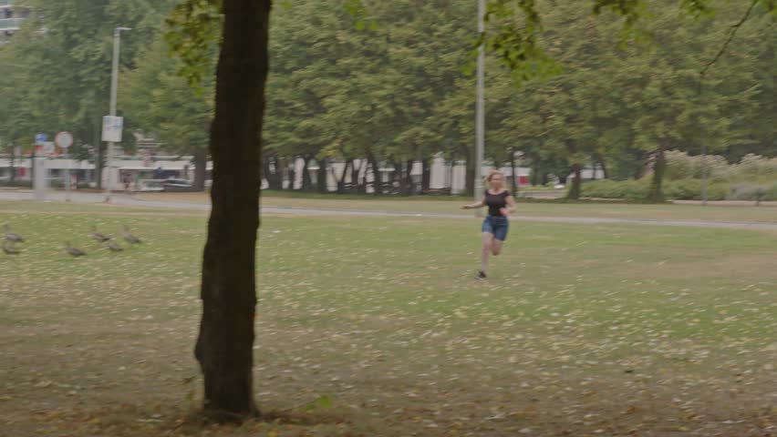 Scared woman running through a park and tripping while being chased by two criminals