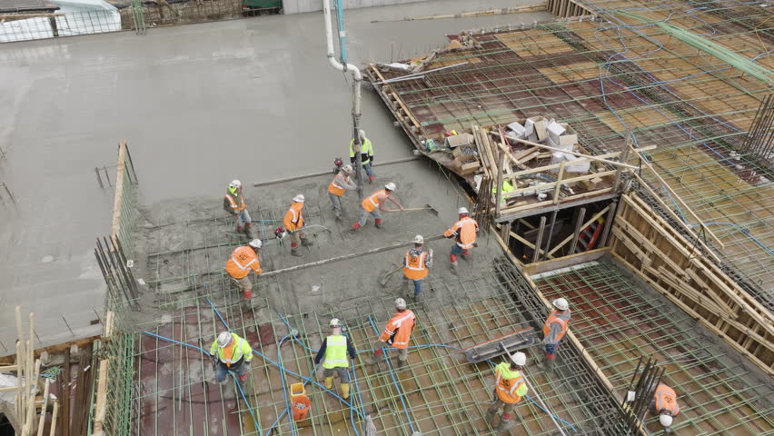 Aerial, blue collar workers pumping concrete on building foundation