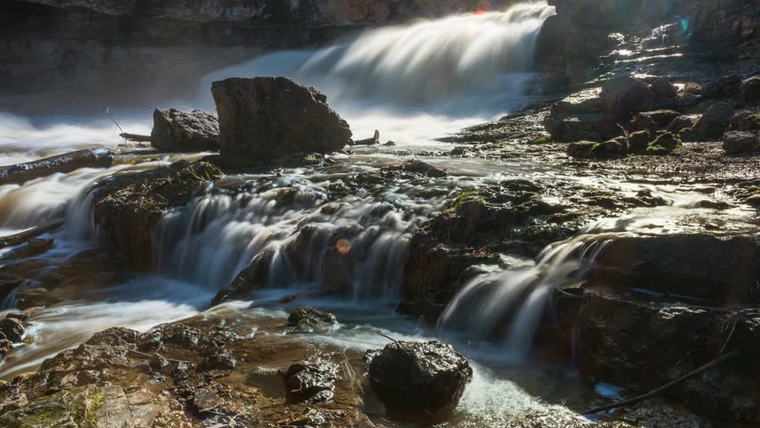 Timelapse of smooth waterfall stream flowing down rocks during the day