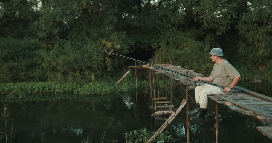 Mature man fishing on a wooden dock at river