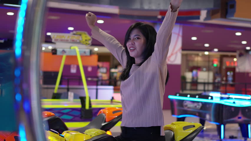 Beautiful young asian woman enjoy playing moto bike arcade game in game center, Hobby and leisure lifestyle on weekend or vacation.