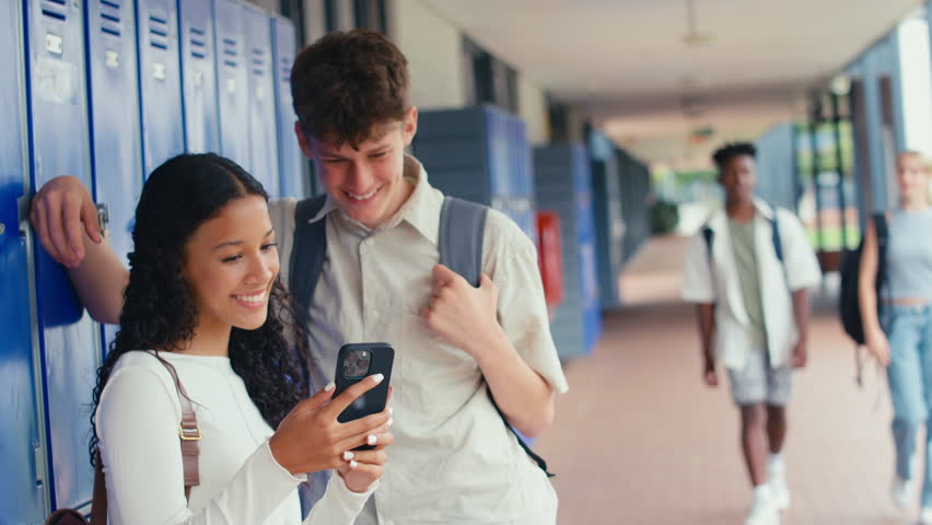 Two high school or secondary students looking at social media or internet on mobile phone by lockers - shot in slow motion