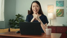 Happy attractive young Asian woman using laptop talk video conference call with friends or family. Beautiful female smile looking at laptop computer screen talking sit at desk in living room
