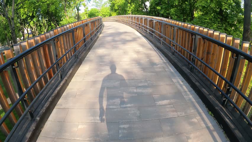 First-person view. A runner runs on a morning jog on the street in the park over a bridge. A shadow falls on the ground Royalty-Free Stock Footage #1103876221