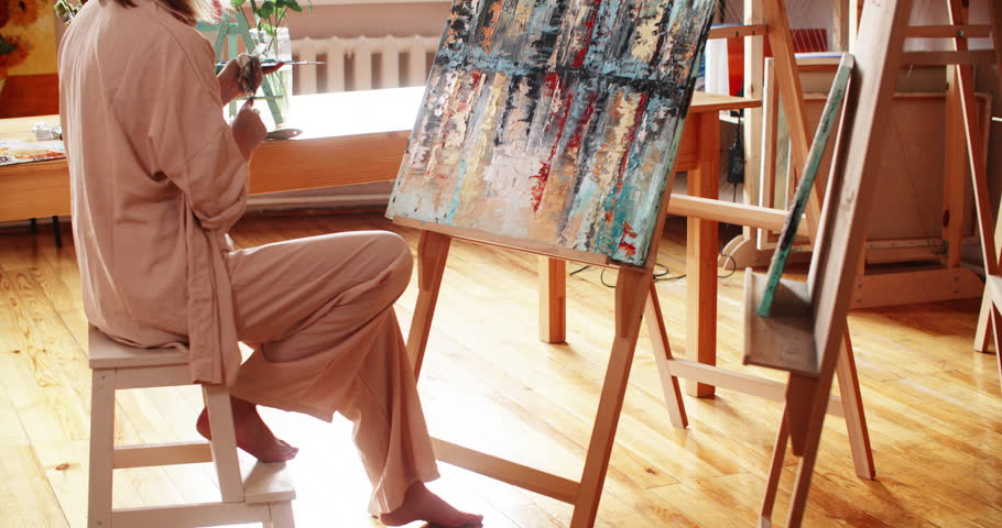 Artist painter woman painting abstract emotional colorful picture using oil paints in art workshop with spatula. Contemporary art, fine art. Creative female paintress works in art studio on artwork.