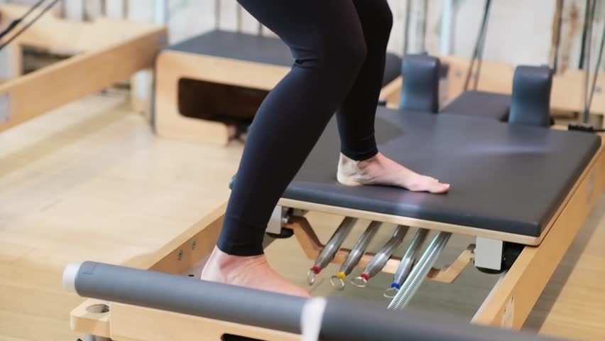Intensive pilates workout in modern studio woman in sportswear strengthening leg muscles standing on reformer female person enjoying sports activity in morning Royalty-Free Stock Footage #1103880511
