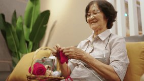 Happy elderly Asian woman grandmother sitting on sofa knitting with needles and red thread in living room. Retired old woman relax and enjoy indoor lifestyle leisure activity hand craft hobby at home. - Powered by Shutterstock - Get 15% off with code: PIKWIZARD15