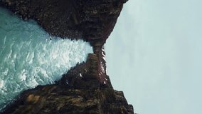 Vertical video: Drone shot of gullfoss waterfall canyon, amazing icelandic nature with huge river stream and massive rocky hills. Spectacular cascade in iceland running down off cliff. Slow motion.