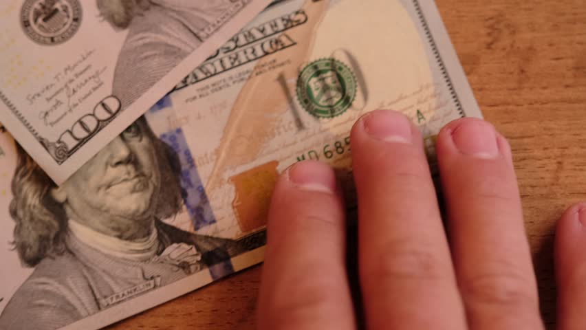 Man's hand take a hundred dollar bill from the table close up. American banknotes value of 100 simbols. Cash of hundred dollar bills.