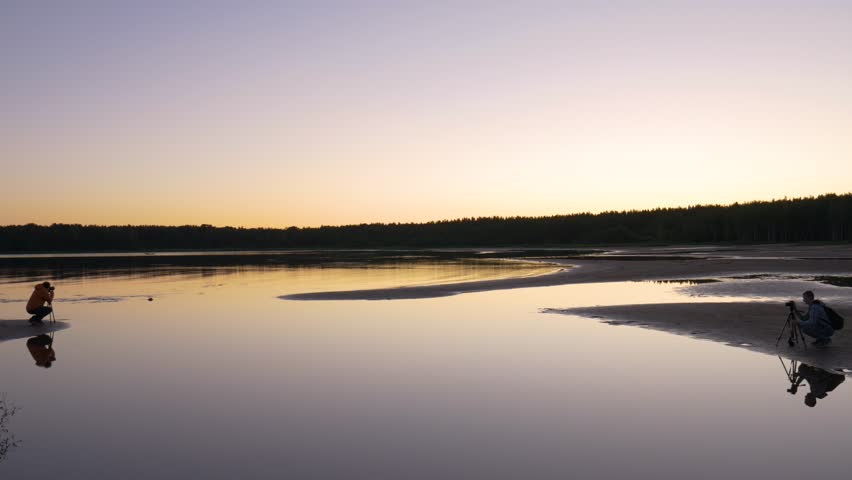 Two cameramen shoot the sunset on the lake. The work of videographers on the water.
