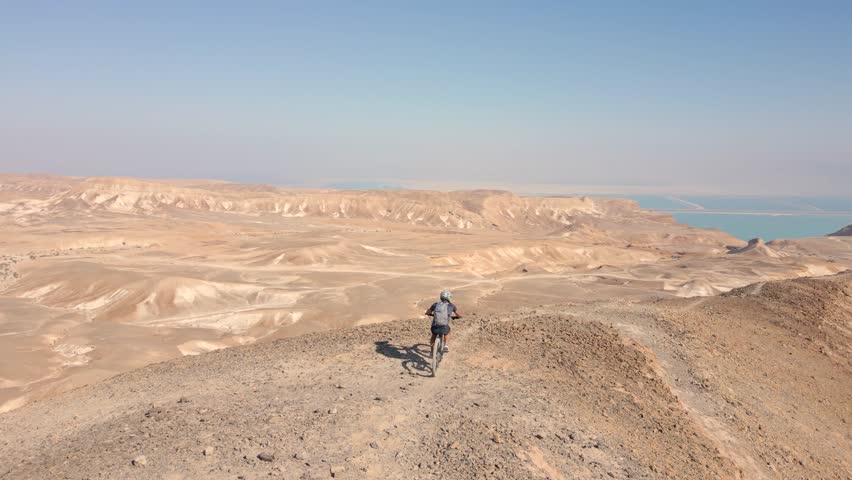Mountain Biking Downhill steep narrow rocky ridges with scenery in the wild alone near the Dead Sea lake and Arad Mountains in the Negev Desert, Israel with bright blue sky Aerial Active Track Follow	