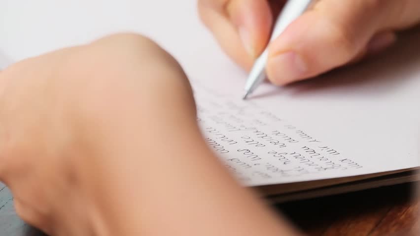 closeup of a hand in the upper right corner journaling in a white notebook on a wooden table with the other hand blurry in the foreground. Royalty-Free Stock Footage #1103902225