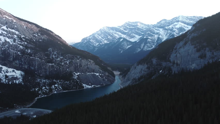 Orbiting aerial drone shot of a lake nestled below snowy and beautiful Canadian peaks near Canmore, Alberta