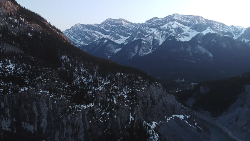 Orbiting aerial drone shot of snowy and beautiful Canadian peaks near Canmore, Alberta during golden hour at sunset