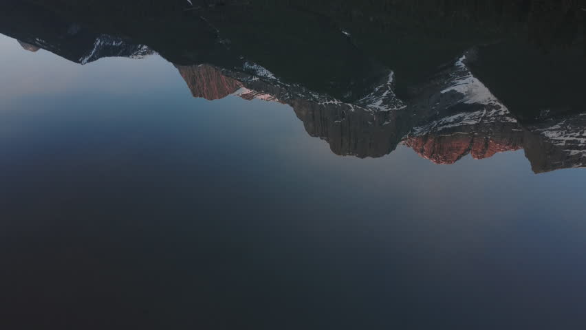 Pan up aerial drone shot over water and a reflection of snowy and beautiful Canadian peaks near Canmore, Alberta at sunrise