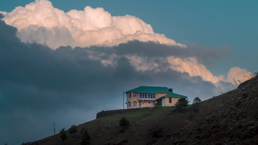 timelapse of clouds floating over a solitary house nestled in the mountains