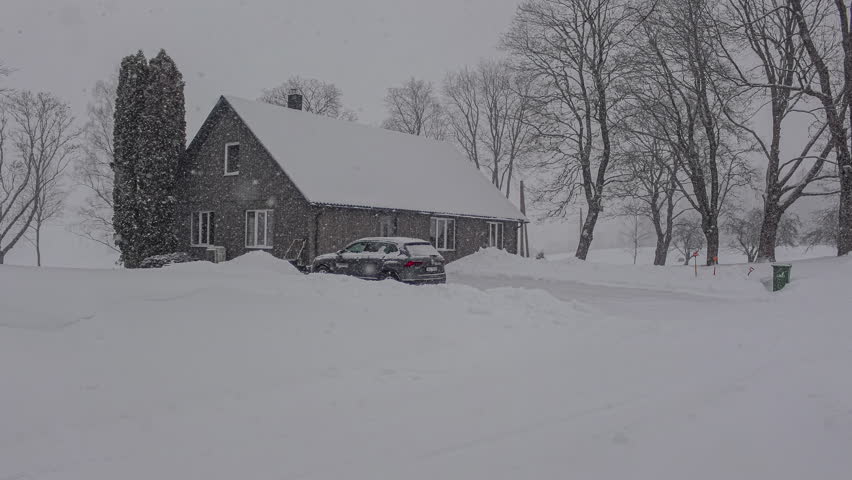 Timelapse shot of heavy snow falling on a wooden cabin house throughout a cloudy snowy winter day.