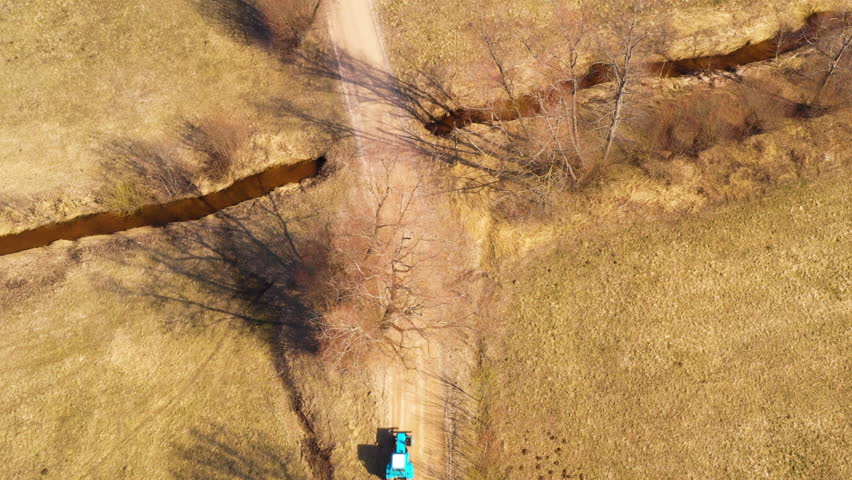 Blue tractor pulling trailer with chopped wood on rural country road, aerial downwards view