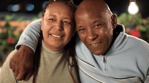 Happy african senior couple having fun smiling on camera and hugging together during night time at house terrace outdoor  Stockvideó